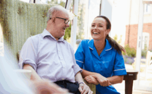 Carer in a blue uniform, smiling and laughing with a service users. Voices of Care campaign