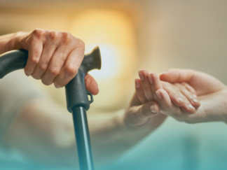 Consistency in care, blog post featured image, holding hands with a service user using their walking stick to get up