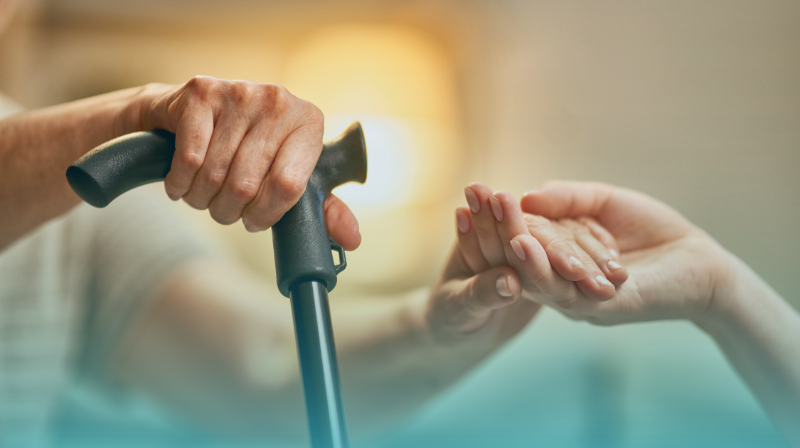 The Importance Of Consistency In Care - Universal Care Services Consistency In Care, Blog Post Featured Image, Holding Hands With A Service User Using Their Walking Stick To Get Up